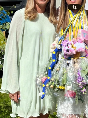 Ljusgrön kortklänning - Långärmad klänning med lös passform. Klänningen är grön, kort och plisserad. Den har knäppning bak, rund halsringning, voluminös ärm och vågiga kanter. Använd 2 gånger