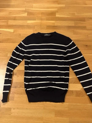 Marinblå randig tröja från Dressmann - Säljer en marinblå tröja från Dressmann i storlek S. Tröjan har vita horisontella ränder och är långärmad med rund hals. Perfekt för dig som gillar klassisk och stilren look. Materialet känns mjukt och bekvämt, troligen bomull eller bomullsblandning.