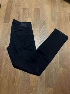 Svarta skinny jeans från Lee Luke - Säljer ett par svarta skinny jeans från Lee med klassisk femficksdesign och diskret Lee-logga på bakfickan. Jeansen har smal passform och är tillverkade i stretchig bomullsblandning för extra komfort. Perfekta till sneakers eller boots.