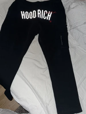Svarta mjukisbyxor från Hoodrich - Svarta mjukisbyxor från Hoodrich med stor vit logga över Framdelen. Byxorna har en ficka på sidan av benet och är tillverkade i mjukt material. Har hela setet av mjukibyxorna om ni är intresserade. Dem är helt nya.