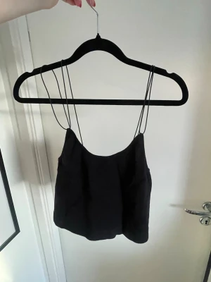 Svart croppad linnetopp med tunna band - En svart croppad ribbad linnetopp med tunna axelband från Gina Tricot 