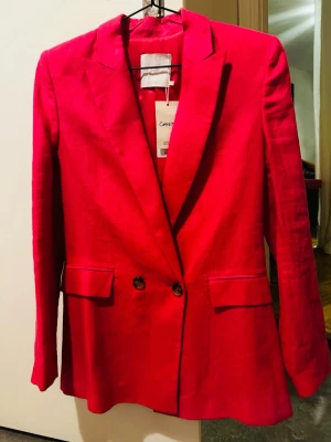 Rosa kavaj från Common Threads - Snygg rosa kavaj från mango i rak passform med dubbelknäppning framtill och klassiska slag. Tillverkad i 100%  linnematerial, perfekt för att lyfta vilken outfit som helst. Fickor med lock och knappar vid ärmslut ger extra stilpoäng.