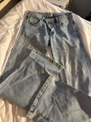 Ljusblå raka jeans med fickdetaljer - Säljer ett par ljusblå jeans från lager157 med raka ben och klassisk femficksdesign. Jeansen har snygga ficklock med knapp bak och normal midja. Perfekta till en avslappnad stil och passar till det mesta. Materialet är klassisk denim i bomull.