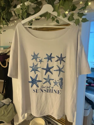 Vit t-shirt med blått tryck från SHEIN - Säljer en vit t-shirt från SHEIN i storlek M med blått tryck av sjöstjärnor och texten 'Soul full of SUNSHINE'. T-shirten har rund hals, korta ärmar och är gjord i mjuk bomull. Perfekt för sommarvibbar och chill dagar.
