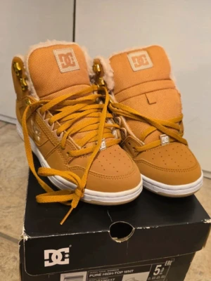 DC Pure High-Top WNT sneakers wheat - Säljer ett par DC Pure High-Top WNT sneakers i färgen wheat. Skorna har högt skaft, snörning med metallhål, vit sula och mjukt foder i syntetpäls. Materialmix av skinn och textil med DC-logga på sidan och plös. Perfekta för dig som vill ha streetstyle med extra värme.