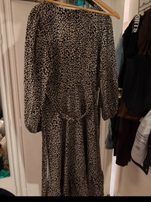 Svartvit mönstrad midiklänning boohoo - Svartvit midiklänning från boohoo med coolt prickigaktigt mönster. Klänningen har v-ringning, långärmad (lite kortare än långärmad)  med resår och ett knytband i midjan för snygg passform. Tillverkad i 100% polyester, perfekt för dig som gillar statement-plagg.