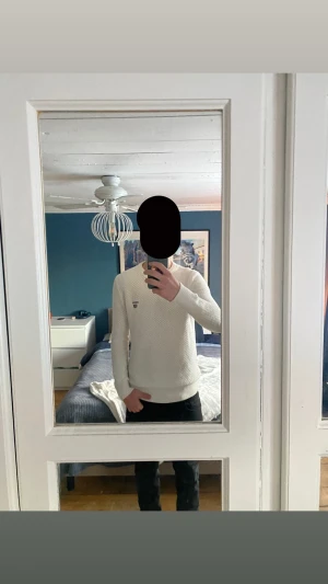 Vit stickad tröja från Morris - Säljer en vit stickad tröja från Morris i storlek M. Tröjan har ett diskret märke på bröstet och är gjord i ett grovt stickat mönster med ribbade muddar vid hals, ärmslut och nederkant. Perfekt för lager-på-lager under höst och vinter.