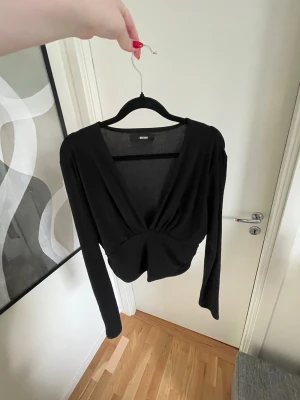 Svart långärmad topp  - En svart långärmad topp från BikBok i storlek L med djup v-ringning. Toppen har en liten croppad passform och twistad detalj framtill 
