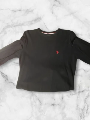Svart stickad tröja från U.S. Polo Assn - Säljer en svart stickad tröja från U.S. Polo Assn i storlek S. Tröjan har rund halsringning med ribbad kant och en röd broderad logga på bröstet. Klassisk och enkel design som passar till det mesta.