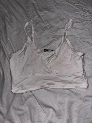 Vit omlott linnetopp från FB Sister - Säljer en vit omlott linnetopp från FB Sister i storlek M. Toppen har smala axelband, omlottdesign framtill och är croppad. Perfekt till sommaren och enkel att matcha med olika stilar.