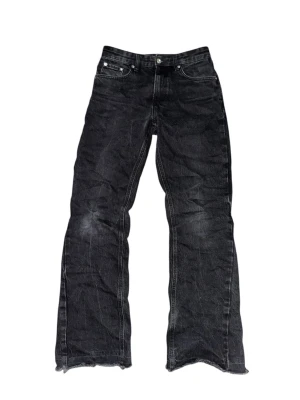 Svarta bootcut jeans - Säljer ett par svarta jeans med bootcut passform och råa, slitna kanter längst ner. Jeansen har klassisk femficksdesign och är tillverkade i kraftigt denimtyg. Perfekta för dig som gillar en avslappnad och edgy stil.