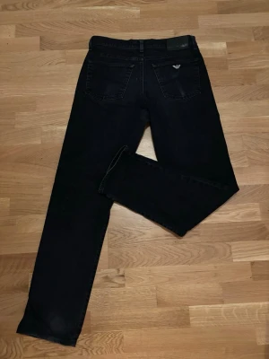 Svarta Armani Jeans straight fit - Säljer ett par svarta jeans från Armani Jeans med klassisk femficksmodell och silverfärgade detaljer. Jeansen har rak passform och är tillverkade i ett mjukt bomullsmaterial med jeansstruktur. Diskret Armani-logga på bakfickan och patch i midjan.