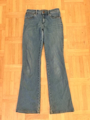 Blå bootcut jeans från Wrangler💖🥹 - Säljer ett par klassiska blå jeans från Wrangler med bootcut passform. Jeansen har fem fickor, ljus tvätt och ikoniska bakfickor med broderad detalj. Tillverkade i slitstark bomull med en bekväm midja och dragkedja framtill. Slitna lite vid vissa ställen