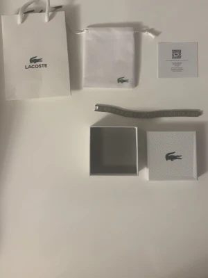 Snyggt silverfärgat armband från Lacoste - Stilrent armband från Lacoste i silverfärgad metall med rutmönstrade länkar och den klassiska krokodilloggan på spännet. Kommer med original ask, påse och certifikat. Perfekt accessoar för dig som gillar en clean och modern look.