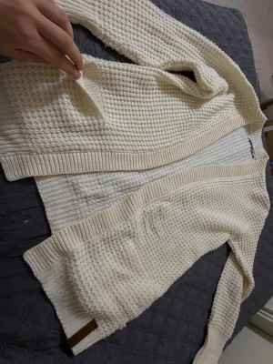 Vit stickad kofta från Denim Makers - Säljer en krämvit, chunky stickad kofta från Denim Makers. Koftan har öppen front, två stora fickor och breda ribbade muddar. Perfekt för lager på lager och riktigt mysig till höst och vinter. Klassisk och enkel design som passar till allt. Den är inte så lång