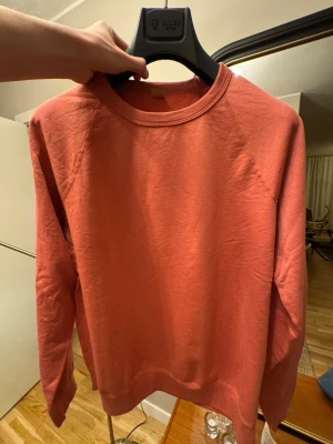 Save Khaki United - Supima Crew  - Sweatshirt – Terra Pink – L - Stilren sweatshirt från Save Khaki United, modell Supima Fleece Crew, i färgen Terra Pink (mjuk rosa/terrakotta-ton).  Tillverkad i 100 % U.S. Supima-bomull, vilket ger en väldigt mjuk, följsam och hållbar kvalitet. Minimalistisk design med raglanärmar och ribbade muddar.  • Storlek L • Made in USA • Supima cotton (premiumbomull) • Klassisk passform • Färg: Terra Pink • Icke använda  Nypris ca 1 000 kr.