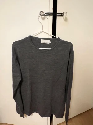 Mörkgrå långärmad tröja Casual Friday - En stilren mörkgrå långärmad tröja från Casual Friday. Tröjan har rund halsringning och är gjord i ett mjukt, tunt material som passar perfekt till lager på lager. Enkel och clean look som funkar till det mesta.