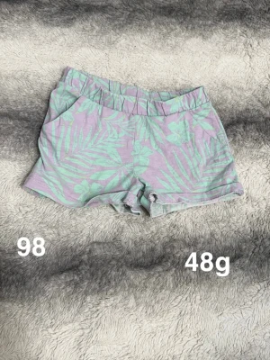shorts med blommönster - Säljer ett par shorts med blommönster och tropiska blad. Shortsen har elastisk midja och uppvikta benslut. Perfekta för varma dagar och riktigt sköna att ha på sig.🌸 Fint använt skick. Storlek 98