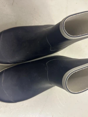 Svarta gummistövlar från Tretorn - Säljer ett par klassiska svarta gummistövlar från Tretorn med vit kant upptill och greppvänlig sula. Insidan är ljus och fodrad med textil för extra komfort. Perfekta för regniga dagar och utflykter.