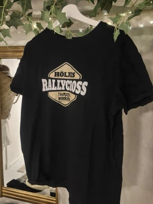 Svart Höljes Rallycross t-shirt Clique - Svart t-shirt från Clique i storlek XL med tryck 'Höljes Rallycross The Magic Weekend' på bröstet. Klassisk rund hals och korta ärmar. Tillverkad i mjuk bomull som känns skön mot huden. Perfekt för dig som gillar motorsport och vill sticka ut.