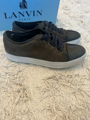 Lanvin sneakers - Lanvin DBB1 cap toe sneakers Storlek: 42 / UK 8 Pris: 999 kr  Beskrivning: Klassiska Lanvin DBB1 cap toe sneakers i svart. Stilren och tidlös modell som passar både vardag och mer uppklädda outfits.  – Storlek: 42 / UK 8 – Ingår: Dustbag – Nypris: ca 5200 kr  Modellen upplevs som något stor i storleken, rekommenderas att gå ner cirka en storlek från sin vanliga.  Kategori: Sneakers Färg: Svart Märke: Lanvin finns lite småslitage 