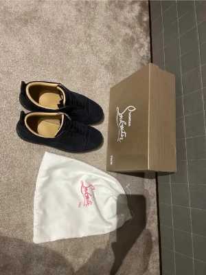 Mörkblå mocka sneakers från Louboutin - Säljer ett par mörkblå sneakers från Christian Louboutin i mjuk mocka med klassiska röda sulor. Skorna har rund tå, svarta snören och beige skinnfoder. Kommer med originalkartong och dustbag med Louboutin-logga. Äkta har kvitto