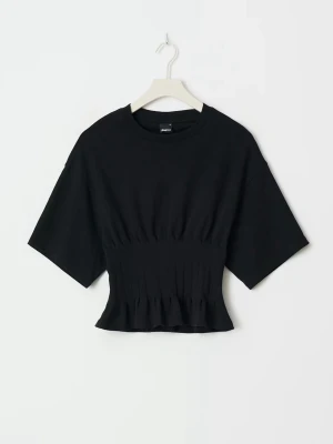 Svart figursydd topp - Säljer en svart croppad topp från gina med korta ärmar och resår i midjan som ger en snygg siluett. Toppen har rund halsringning och är tillverkad i mjuk bomull. Pleated tee från gina. Figursydd topp