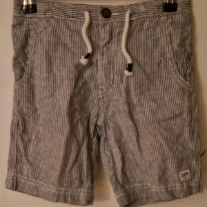 Randiga shorts från H&M L.O.G.G. - Snygga randiga shorts i storlek 122 från H&M L.O.G.G. i vitt och grått. De har snörning i midjan, knappstängning och flera fickor både fram och bak. Tillverkade i mjuk bomull. Hund finns i hemmet. Kolla in mina andra annonser för samfrakt! 
