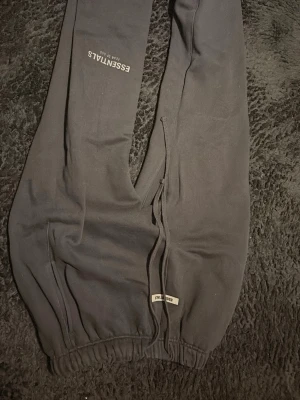 Svarta Essentials mjukisbyxor - Säljer ett par svarta mjukisbyxor från Essentials Fear of God. Byxorna har resår i midjan och benslut, långa snören, sitter bra även på folk i storlek L 