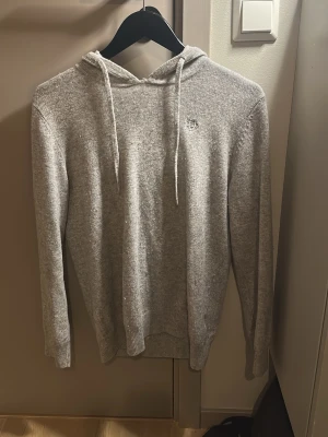 Merinoull tröja med huva - En merinoull tröja med luva i färgen grå, en stilren tröja i bra skick men det finns ett litet problem, man ser det på bild 3 men det går enkelt att laga, en allmänt bra stilren tröja för ungdomar
