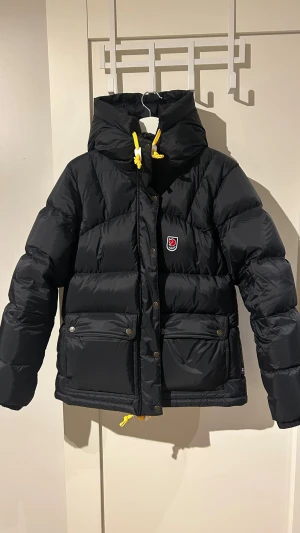 Ny Svart Fjällräven Expedition dunjacka - Säljer en ny svart Fjällräven Expedition down lite  dunjacka för dam. Puffig modell med huva och dragkedja samt tryckknappar. Perfekt för kalla dagar. Köpt för 2 veckor sen på Team Sportia men kände att jag skulle vilja gå ner en storlek. Köpt för 7500. 