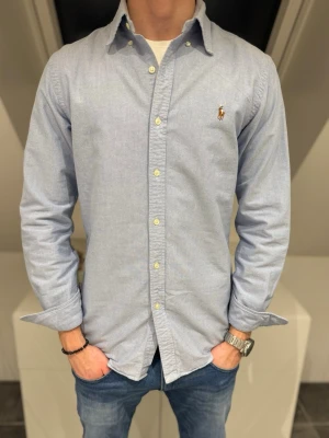 Ljus blå Ralph Lauren skjorta  - Hej nu säljer vi en till Klassisk ljusblå skjorta från Ralph Lauren med button-down krage och broderad logga på bröstet. Skjortan har långa ärmar, normal passform och stängs med vita knappar framtill. Perfekt till jeans eller chinos för en clean look. Storlek M och super skick! Vi säljer den för endast 349kr💯Pris går att gå ner vid snabb och smidig affär! Hör av er vid frågor💙 Studio II Resell 