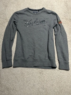 Woolrich tröja - Säljer en skitsnygg grå woolrich tröja med amerikanska flaggan på axeln, den är i nyskick (ingen fading på texten)  köpt för 800 
