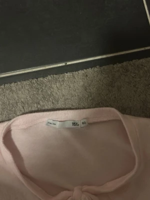 Ljusrosa kofta med knyt framtill - Supersöt ljusrosa kofta med lång ärm och knytband framtill. Koftan är croppad och har en mjuk, lite glansig yta som känns riktigt skön mot huden. Perfekt att slänga över en topp för en söt och enkel look.