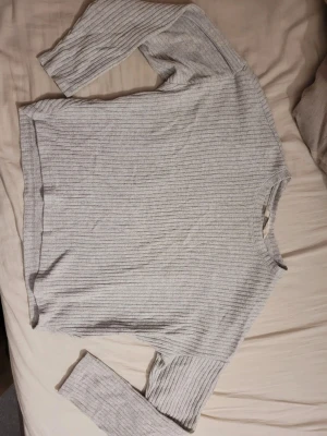 Ljusgrå ribbad långärmad tröja - En stilren ljusgrå långärmad tröja med ribbad struktur. Perfekt för dig som gillar en enkel men snygg look. Tröjan har rund hals och är gjord i ett mjukt material som känns skönt mot huden.