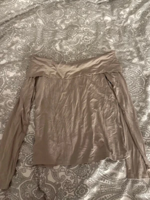 Beige offshoulder topp från 157 - Snygg beige offshoulder topp från 157 i storlek M. Toppen har långa ärmar och en bred, vikt kant upptill som ger en cool och trendig look. Materialet är mjukt och har en lätt glansig finish som känns lyxig. Perfekt att styla med jeans eller kjol.