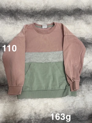 Färgglad sweatshirt i rosa och grön - En snygg sweatshirt med breda block i rosa, ljusgrått och grönt. Tröjan har rund hals, långa ärmar och en stor magficka framtill. Ribbstickade muddar vid ärmslut och nederkant ger en skön passform. Perfekt för dig som gillar färgkombos!🌸 Fint använt skick. Storlek 110