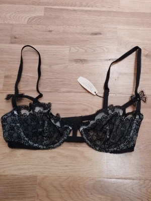 NY Svart spetsbh från Victoria's Secret  - Säljer en svart spets-bh från Victoria's Secret med fantastiskt fina spets-detaljer och strass. Ny med tags inklusive priset. Den amerikanska storleken 32C är som 70C. Den har justerbara band och knäppning bak. Perfekt för alla hjärtans dag  / Valentine's day. Jag har fler annonser uppe och ger mängd rabatt, så kolla gärna min sida!