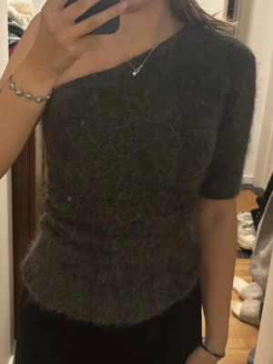 Mörkgrå stickad oneshoulder topp - Säljer en fluffig mörkgrå stickad topp med oneshoulder-design och en kort ärm. Toppen har en mjuk och mysig känsla och sitter snyggt figurnära. Perfekt för dig som vill ha något unikt och trendigt i garderoben.
