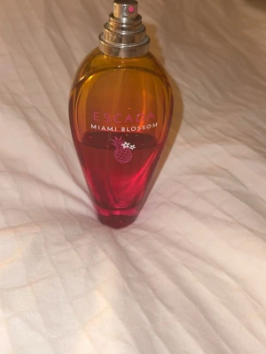 Escada Miami Blossom parfym - Färgstark och trendig parfym från Escada med namnet Miami Blossom. Perfekt för dig som vill ha en fräsch och ungdomlig touch till din stil. Flaskan har en snygg design som sticker ut i badrumsskåpet.
