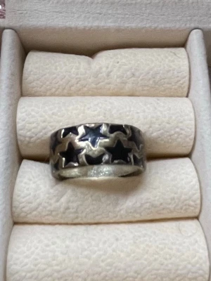 Bred silverfärgad ring med stjärnor - Cool bred ring i silverfärg med svarta stjärnor runt hela ringen. Ringen har en chunky känsla och sticker verkligen ut på fingret. Perfekt för dig som gillar statement-smycken och vill addera lite edge till din stil. Pris kan diskuteras 🥰