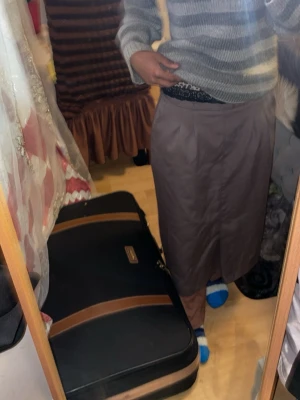 Brun långkjol med slits - Säljer en brun långkjol i rak modell med diskreta veck framtill och en liten slits bak. Kjolen har bred linning och är tillverkad i ett mjukt tyg som känns lite som bomull eller polyester. Perfekt för dig som gillar en enkel och clean stil. Priset kan diskuteras 