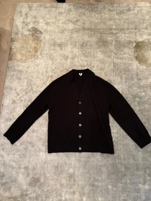 Svart Arket cardigan/kofta - En stilren svart kofta/cardigan från Arket med knappar framtill. Koftan har lång ärm, v-ringad hals och är tillverkad i mjuk bomull. Perfekt att slänga på sig över en t-shirt eller skjorta för en clean look. Nypris 800kr men säljer för 399kr, aldrig använd👌