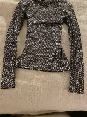 Glittrig långärmad blus Rodebjer - Säljer en superglittrig långärmad topp från Rodebjer. Toppen är täckt av små silverfärgade paljetter på svart botten och har en tight passform. Perfekt för att sticka ut på nästa fest eller event. Materialet känns stretchigt och följsamt. På sidan av innearmen har vissa paljetter trillat av annars ser den ut som ny!