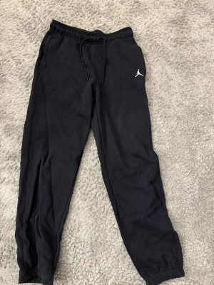 Svarta Jordan mjukisbyxor med logga - Säljer ett par svarta mjukisbyxor från Jordan i storlek S. Byxorna har dragsko i midjan, resår vid bensluten och den klassiska Jumpman-loggan broderad på vänster lår. Perfekta för chill eller träning, tillverkade i mjukt bomullsmaterial. De är i bra skick och har inga fläckar eller något som är sönder. Säljer dessa endast för att de är lite för korta för mig och jag är 167cm lång! 