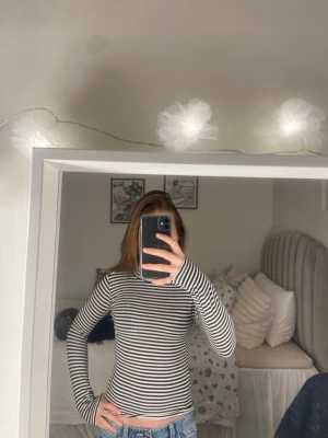 Randig svartvit polotopp - Säljer en långärmad polotopp med svarta och vita horisontella ränder. Toppen har en tight passform och hög krage som ger en clean och stilren look. Perfekt att styla med jeans eller kjol för en enkel men snygg outfit.