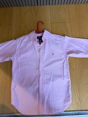 Rosa skjorta från Ralph Lauren - Klassisk rosa skjorta från Ralph Lauren med button-down krage och broderad logga på bröstet. Skjortan har långa ärmar, vita knappar framtill och är gjord i mjuk bomull. Perfekt för en clean och stilren look.