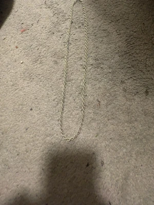 Silverfärgad tvinnad kedja - Säljer en stilren silverfärgad kedja med tvinnad design. Kedjan har en klassisk karbinhake och är stämplad med 925, vilket betyder att den är i äkta silver. Perfekt accessoar för att lyfta din outfit.