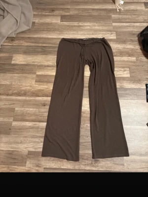 Bruna mjukisbyxor från Nelly - Mysiga bruna mjukisbyxor från Nelly med breda ben och dragsko i midjan. Tillverkade i mjukt material som känns skönt mot huden. Perfekta för chill dagar eller när du vill ha det extra bekvämt.