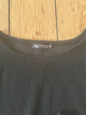 Svart ribbad croppad topp från Zara - En svart croppad topp från Zara med lång ärm och rund halsringning. Toppen är ribbad och har en stilren, enkel design som passar till många olika outfits. Perfekt för dig som gillar en clean och modern look.